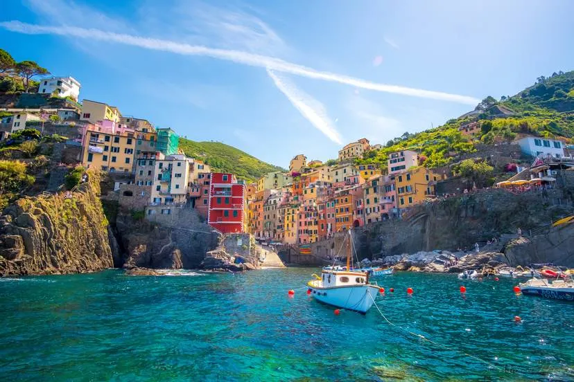 a small boat in the water looks up toward the colorful hillside town of Riomaggiore, Italy